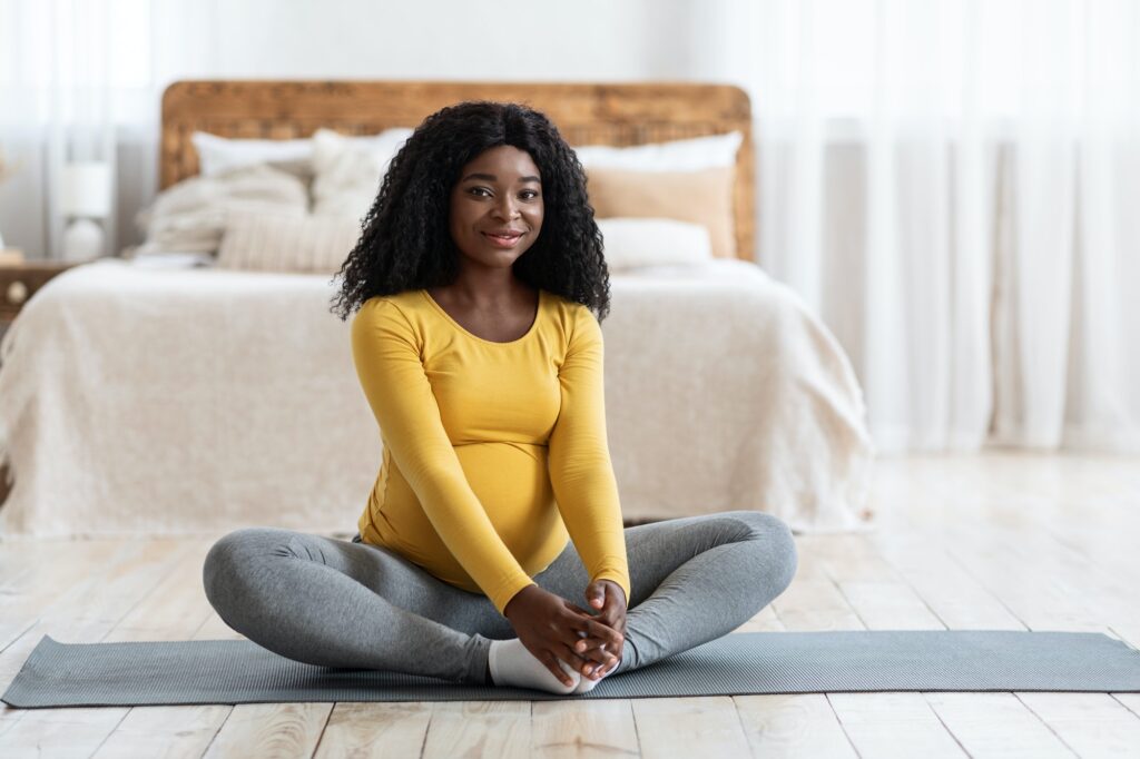 Happy black pregnant lady stretching at home